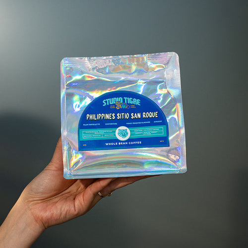 Hand holding a holographic coffee bag with text against a dark background
